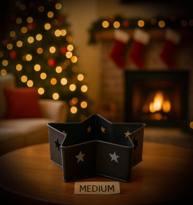 Medium-sized black tin star pan with a rough textured finish, displayed on a wooden table in a Christmas living room for size comparison.