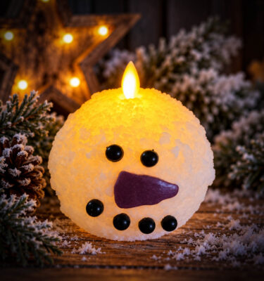 Small Flameless Frosty Snowball Candle, 4 inches, with glowing LED flame, cheerful snowman face and textured snowy finish on a rustic winter display.