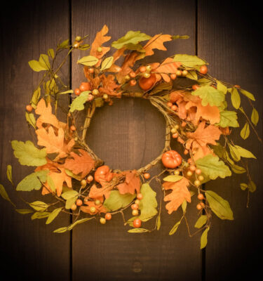 Fall pumpkin wreath decorated with colorful leaves, vines, berries, and small pumpkins, hanging on a rustic wooden door for autumn décor.