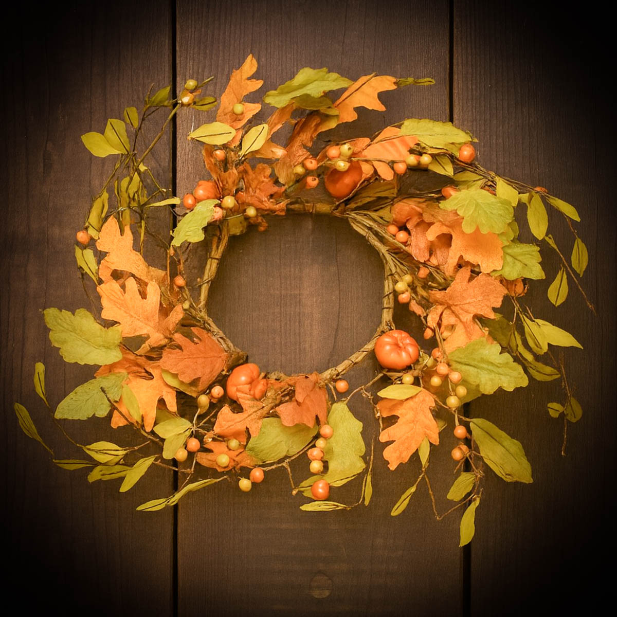 Fall pumpkin wreath decorated with colorful leaves, vines, berries, and small pumpkins, hanging on a rustic wooden door for autumn décor.
