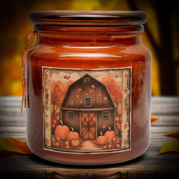 Amber jar candle with a folk art red barn label, featuring pumpkins and fall leaves.