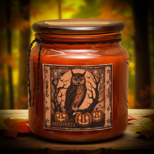 Amber jar candle with a primitive folk art owl label, surrounded by pumpkins and fall leaves.