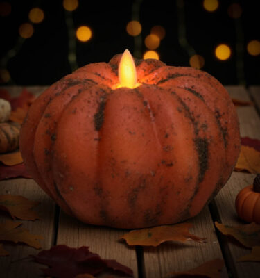 “Small pumpkin moving flame candle with rustic cinnamon spice grunge, glowing on wood table with autumn leaves”