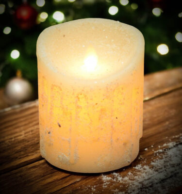 Small 3x4 drizzled white moving flame pillar candle glowing warmly with rustic Christmas décor in the background