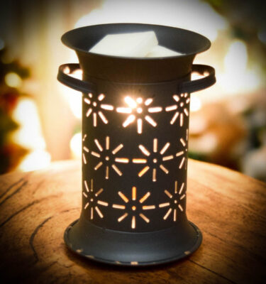 Smokey black punched-tin starburst wax warmer glowing from within, melting wax in the removable top pan.