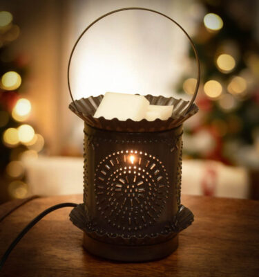 Handcrafted kettle-black jumbo tart warmer with chiseled punched-tin design, glowing from within and warming a wax melt in the removable top pan.