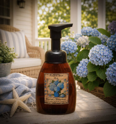 Heavenly Hydrangea foaming soap displayed on a coastal cottage porch surrounded by blooming blue hydrangeas and soft blue linens.