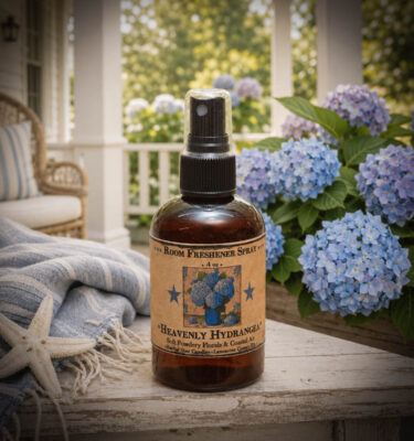 Heavenly Hydrangea room spray displayed on a coastal cottage porch surrounded by blooming blue hydrangeas and soft blue linens.