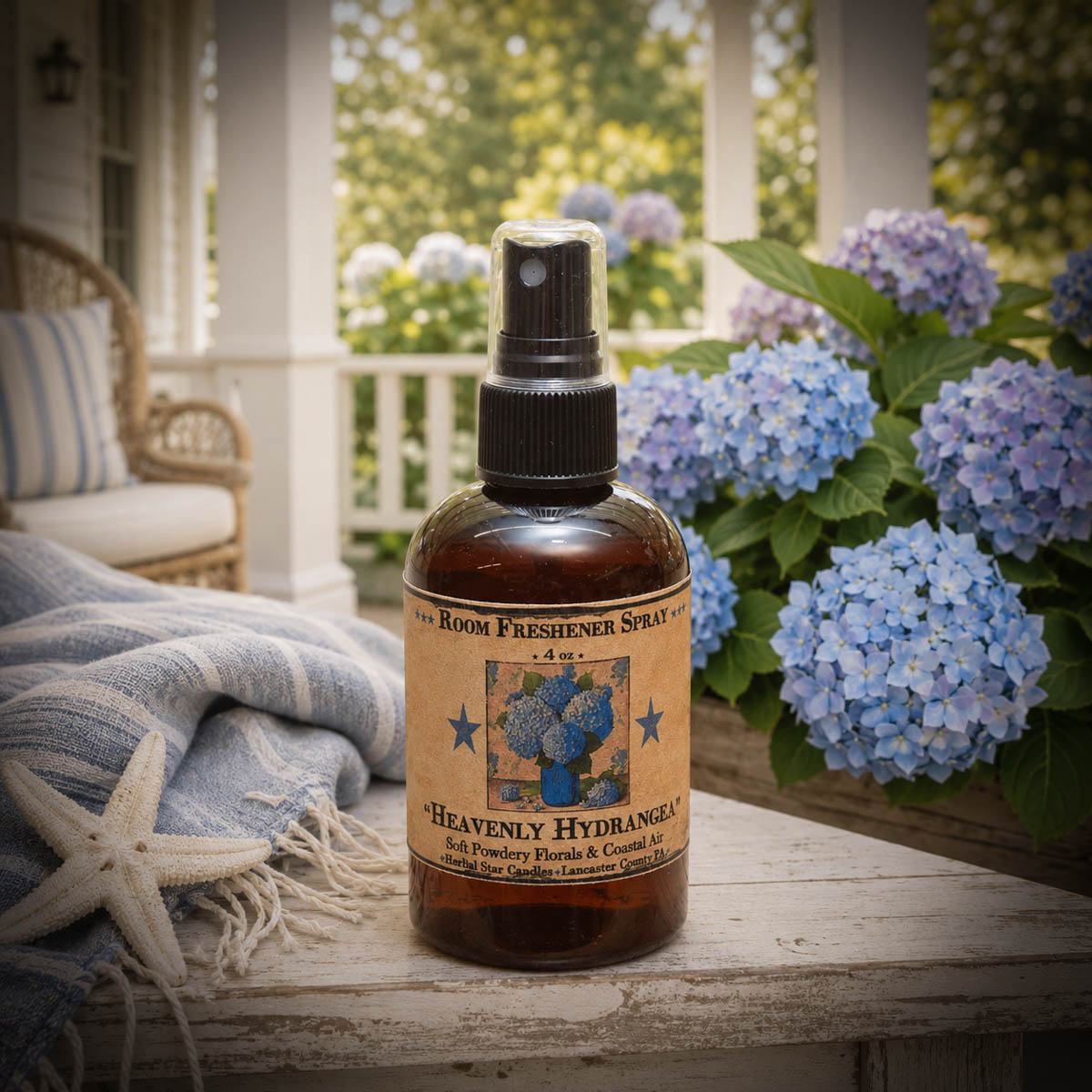Heavenly Hydrangea room spray displayed on a coastal cottage porch surrounded by blooming blue hydrangeas and soft blue linens.