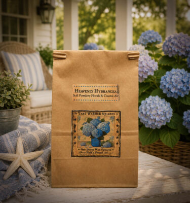 Heavenly Hydrangea wax tart melters in a 10 oz bag displayed on a coastal cottage porch surrounded by blooming blue hydrangeas.